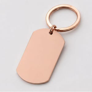 Close-up product photo of a blank rose gold stainless steel keychain with a smooth polished finish. The dog-tag-style pendant is attached to a matching rose gold key ring and displayed on a clean light-gray background, highlighting the customizable engraving area for personalized handwriting, fingerprint, memorial messages, names, dates, logos, or custom text.