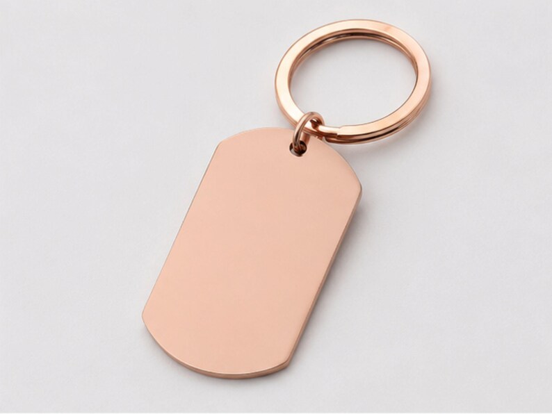 Close-up product photo of a blank rose gold stainless steel keychain with a smooth polished finish. The dog-tag-style pendant is attached to a matching rose gold key ring and displayed on a clean light-gray background, highlighting the customizable engraving area for personalized handwriting, fingerprint, memorial messages, names, dates, logos, or custom text.