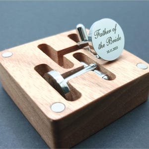Round silver cufflinks engraved with the words “Father of the Bride” and the date “10.11.2025,” displayed on a wooden presentation box.