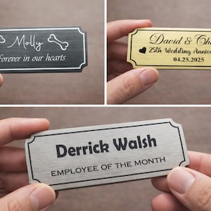 Close-up of hands holding three engraved metal nameplates: a black memorial pet plaque reading “Molly – Forever in our hearts” with bone icons, a gold anniversary plaque for “David & Cheryl – 25th Wedding Anniversary – 04.25.2025” with heart symbols, and a silver “Derrick Walsh – Employee of the Month” plate, all with decorative borders.