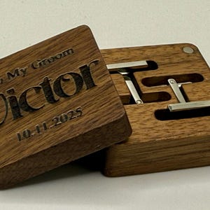 Puede incluir: Una caja de gemelos de madera con la inscripci&oacute;n "To My Groom Victor 10.11.2025" grabada en la tapa. La caja est&aacute; abierta, revelando dos gemelos plateados. La caja es de madera oscura.