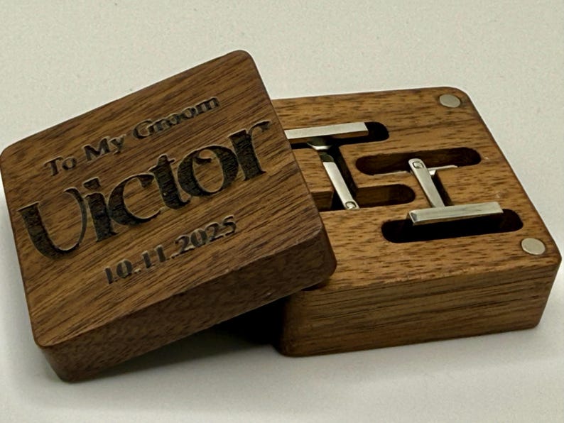 Puede incluir: Una caja de gemelos de madera con la inscripci&oacute;n "To My Groom Victor 10.11.2025" grabada en la tapa. La caja est&aacute; abierta, revelando dos gemelos plateados. La caja es de madera oscura.