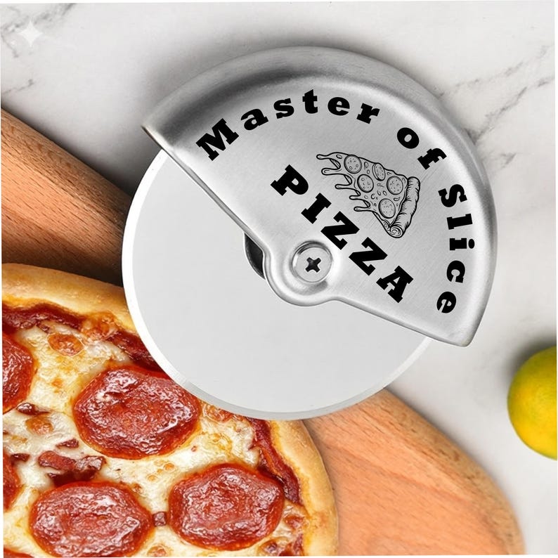 Close-up of a stainless steel pizza cutter engraved with “Master of Slice Pizza” and a pizza slice illustration, positioned over a wooden board beside a pepperoni pizza on a light marble surface.
