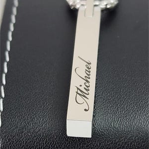 Close-up of engraved silver bar pendant showing personalized name detail and smooth polished finish.