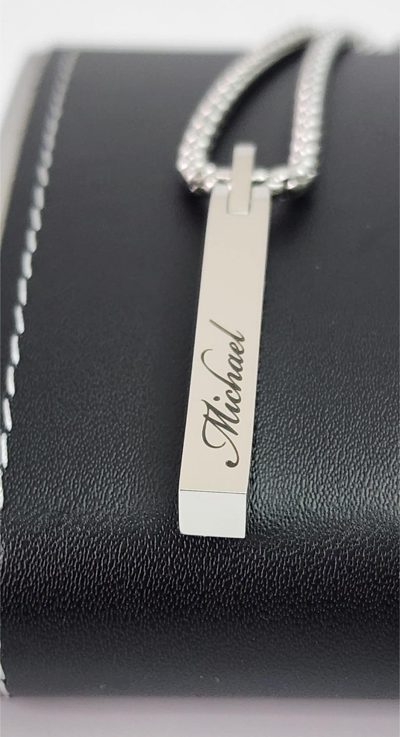 Close-up of engraved silver bar pendant showing personalized name detail and smooth polished finish.