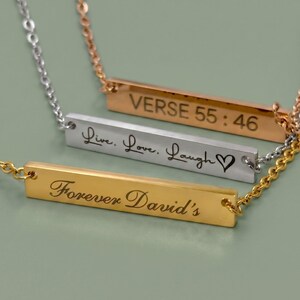 Three personalized horizontal bar necklaces in 18k Gold, Polished Silver, and Rose Gold finishes. The bars are custom engraved with a Bible verse, the phrase "Live, Love, Laugh" with a heart, and "Forever David's" in elegant script fonts.
