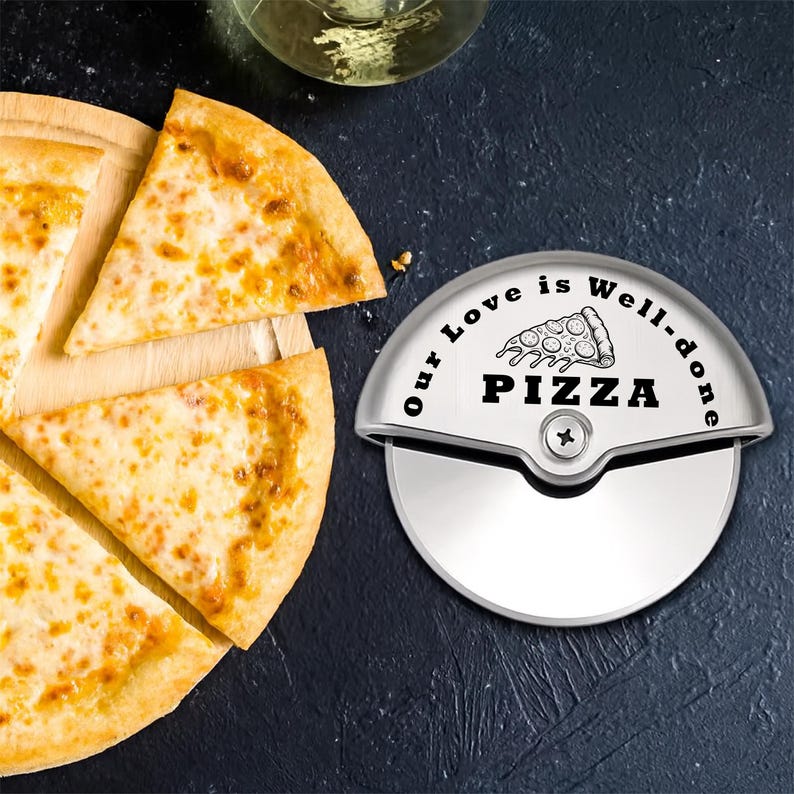 A pizza cutter with the text "I Love Every Pizza" and a pizza slice graphic. The cutter is silver and has a circular blade. Sliced pizza on a wooden board is next to the cutter.