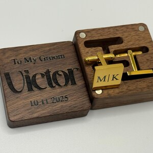 Puede incluir: Una caja de madera marr&oacute;n grabada con "To My Groom", el nombre "Victor" y la fecha "10.11.2025". En el interior, gemelos dorados con las iniciales "M|K" se presentan. La caja est&aacute; abierta.