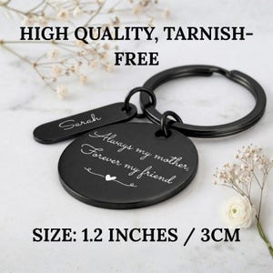 Black personalized keychain for mom with engraved message “Always my mother, forever my friend” and custom name tag, labeled high quality and tarnish-free, size 1.2 inches (3 cm), displayed on a marble background with delicate flowers.