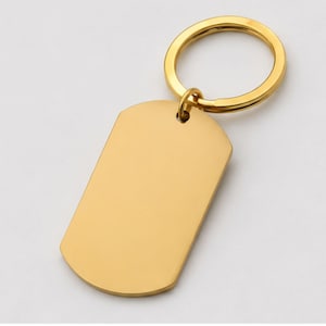 Close-up product photo of a blank gold stainless steel keychain with a polished finish. The dog-tag-style pendant is attached to a matching gold key ring and displayed on a clean light-gray background, showcasing the customizable engraving area for personalized handwriting, fingerprint, memorial, or text engraving.
