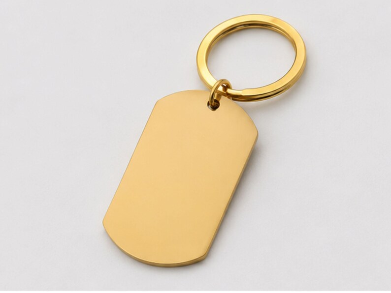 Close-up product photo of a blank gold stainless steel keychain with a polished finish. The dog-tag-style pendant is attached to a matching gold key ring and displayed on a clean light-gray background, showcasing the customizable engraving area for personalized handwriting, fingerprint, memorial, or text engraving.