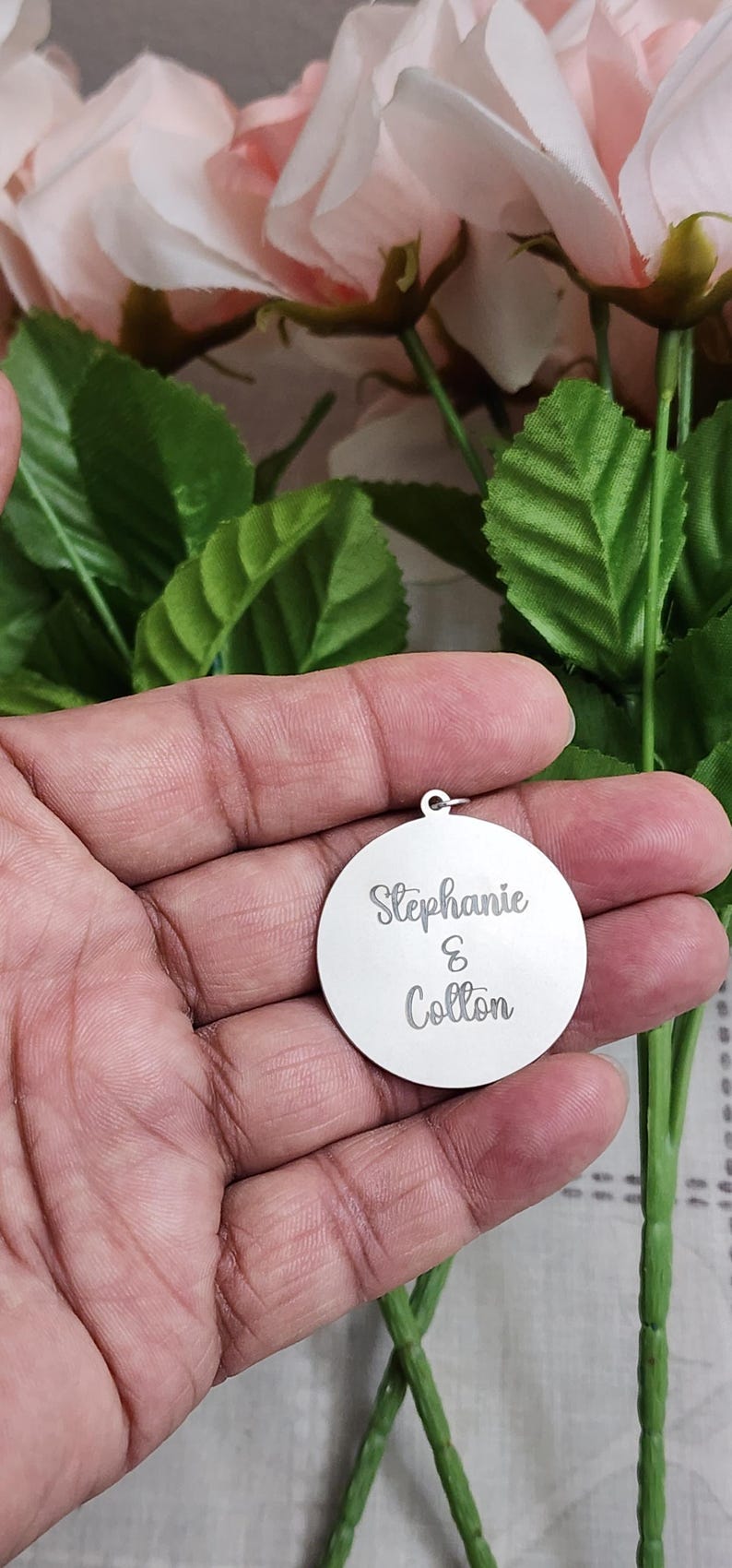 K&ouml;nnte beinhalten: Ein runder Anh&auml;nger aus silberfarbenem Metall mit der eingravierten Aufschrift Stephanie & Colton in Schreibschrift. Der Anh&auml;nger verf&uuml;gt &uuml;ber einen kleinen Verbindungsring an der Oberseite zur Befestigung und hat eine glatte, reflektierende Oberfl&auml;che.