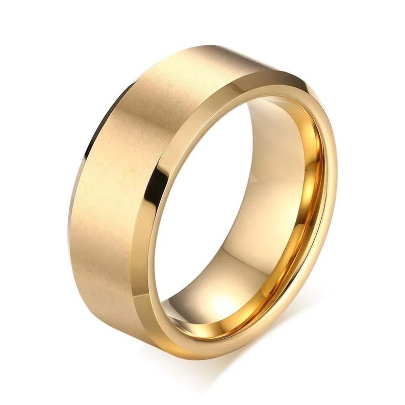 A gold-colored ring with a flat top and beveled edges. The ring has a polished interior and a matte finish on the exterior, reflecting light. This piece of jewelry is suitable for everyday wear.