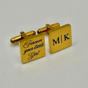 Puede incluir: Gemelos cuadrados dorados. Un gemelo presenta el texto "Forever your little Girl" en escritura cursiva. El otro gemelo muestra las iniciales "M|K" en negro. Los gemelos tienen un poste rectangular y una palanca redondeada.