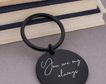 May include: A round black metal keychain featuring a split ring and a circular pendant. The pendant is engraved with the white cursive text "You are my always" centered on its surface. The keychain has a smooth matte finish and a simple design.