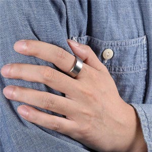 A gold-colored ring with a flat top and beveled edges. The ring is worn on a finger, showcasing its simple, modern design. The ring's surface has a matte finish, reflecting light subtly.