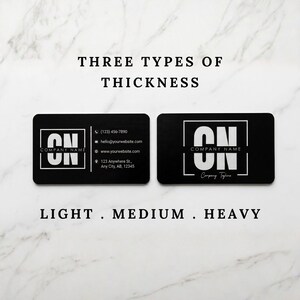 Comparison of metal business card thickness options labeled light, medium, and heavy on a marble background