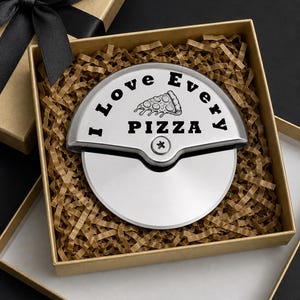 Stainless steel pizza cutter engraved with “I Love Every Pizza” and a pizza slice illustration, neatly placed in a gold gift box with brown crinkle paper filler and a black ribbon lid.