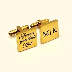 Gold-toned square cufflinks. One cufflink features the text "Forever your little Girl" in cursive script. The other cufflink displays the initials "M|K" in a bold, black font. The cufflinks have a classic, elegant design.
