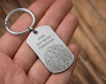 May include: A silver-toned metal dog tag keychain featuring a circular split ring. The tag is engraved with the text GONE BUT NEVER FORGOTTEN and a detailed black fingerprint design centered on the smooth, rectangular surface with rounded corners.