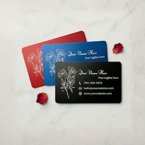 Custom engraved metal business cards with floral design in black, blue, and red, shown on marble background with rose petals.