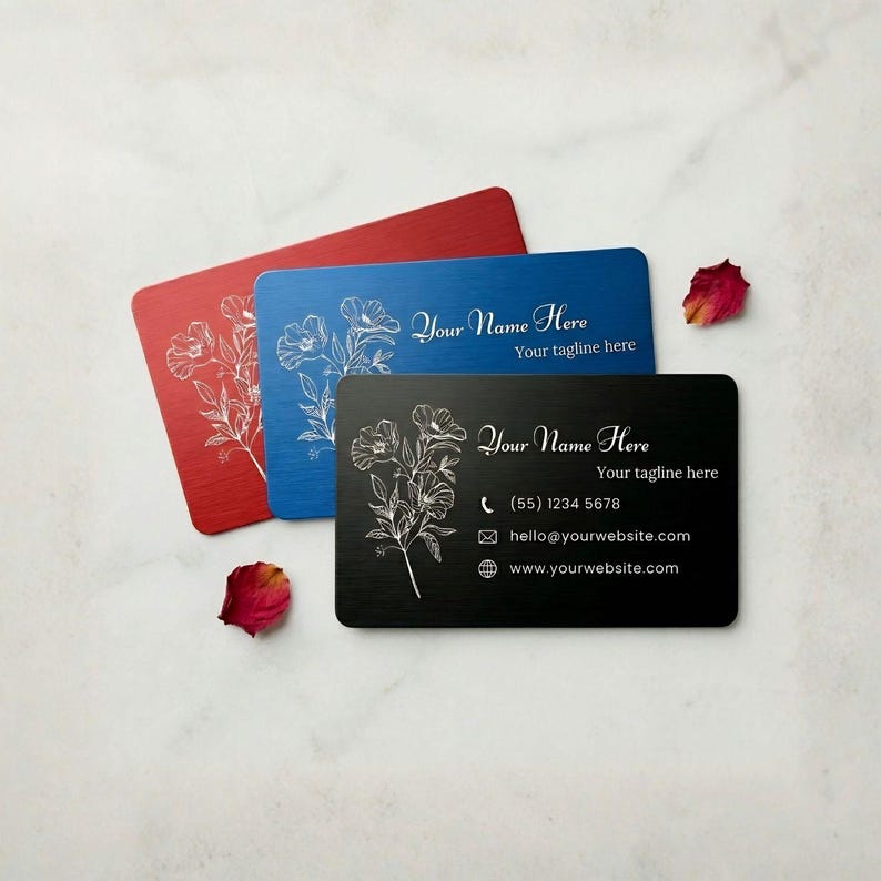 Custom engraved metal business cards with floral design in black, blue, and red, shown on marble background with rose petals.