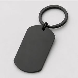 Close-up product photo of a blank black stainless steel keychain with a sleek matte finish. The dog-tag-style pendant is attached to a matching black key ring and displayed on a clean light-gray background, highlighting the smooth engraving surface for custom handwriting, fingerprint, memorial message, logo, or personalized text engraving.