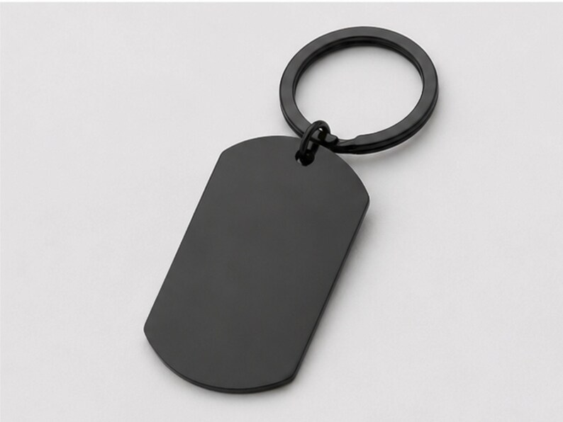 Close-up product photo of a blank black stainless steel keychain with a sleek matte finish. The dog-tag-style pendant is attached to a matching black key ring and displayed on a clean light-gray background, highlighting the smooth engraving surface for custom handwriting, fingerprint, memorial message, logo, or personalized text engraving.