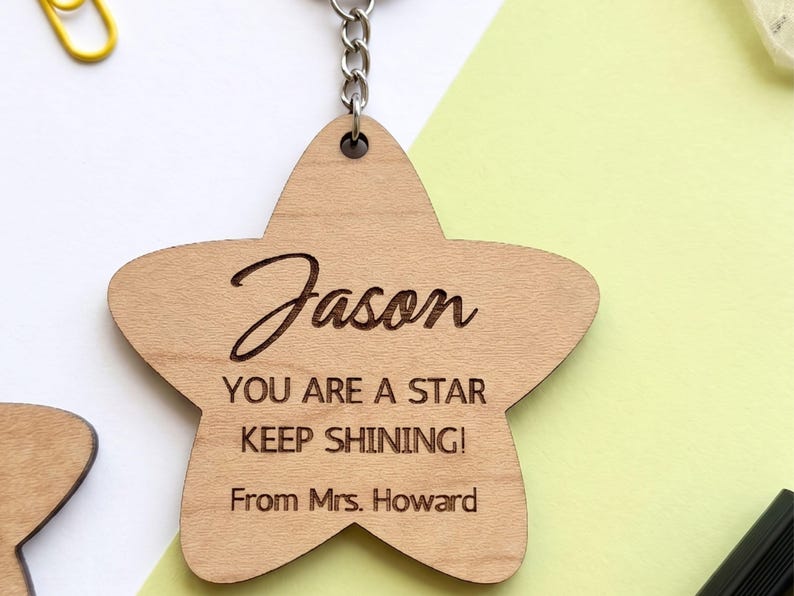 Laser-cut wooden star-shaped keychain engraved with the name "Jason" in script lettering and the message "YOU ARE A STAR KEEP SHINING! From Mrs. Howard." The keychain is attached to a metal chain and displayed on a clean white and pastel green background, photographed in a flat-lay style.