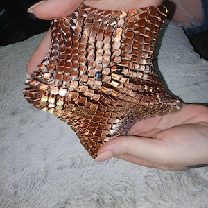 May include: A copper-colored metal mesh sculpture with a geometric, star-shaped design. The sculpture is made of many small, interconnected pieces of metal.