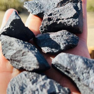 Puede incluir: Una colección de seis piedras de color gris oscuro, con textura rugosa. Las piedras son de varios tamaños y formas, y tienen un brillo metálico.