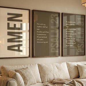 May include: Three framed wall art pieces with text. The first frame reads "AMEN" in large, bold letters. The other two frames display verses from Psalms 23 and 91. The frames are dark brown, and the background is a neutral colour.