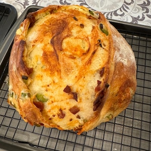 May include: A golden brown loaf of bread with green peppers and bacon baked into the dough. The bread is sitting on a wire rack.