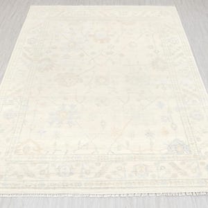 Könnte beinhalten: Cremefarbener rechteckiger Teppich mit detailliertem Blumenmuster und Fransenrand. Der Teppich hat ein zentrales Design mit einem Rand und zeigt eine traditionelle Ästhetik. Die Abmessungen des Teppichs sind nicht sichtbar.
