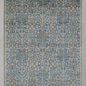 May include: A rectangular rug with a detailed, symmetrical pattern in shades of blue and beige. The rug measures 9x12 ft. The design features stylized floral and geometric elements, creating a classic and elegant look. The rug has a beige border.