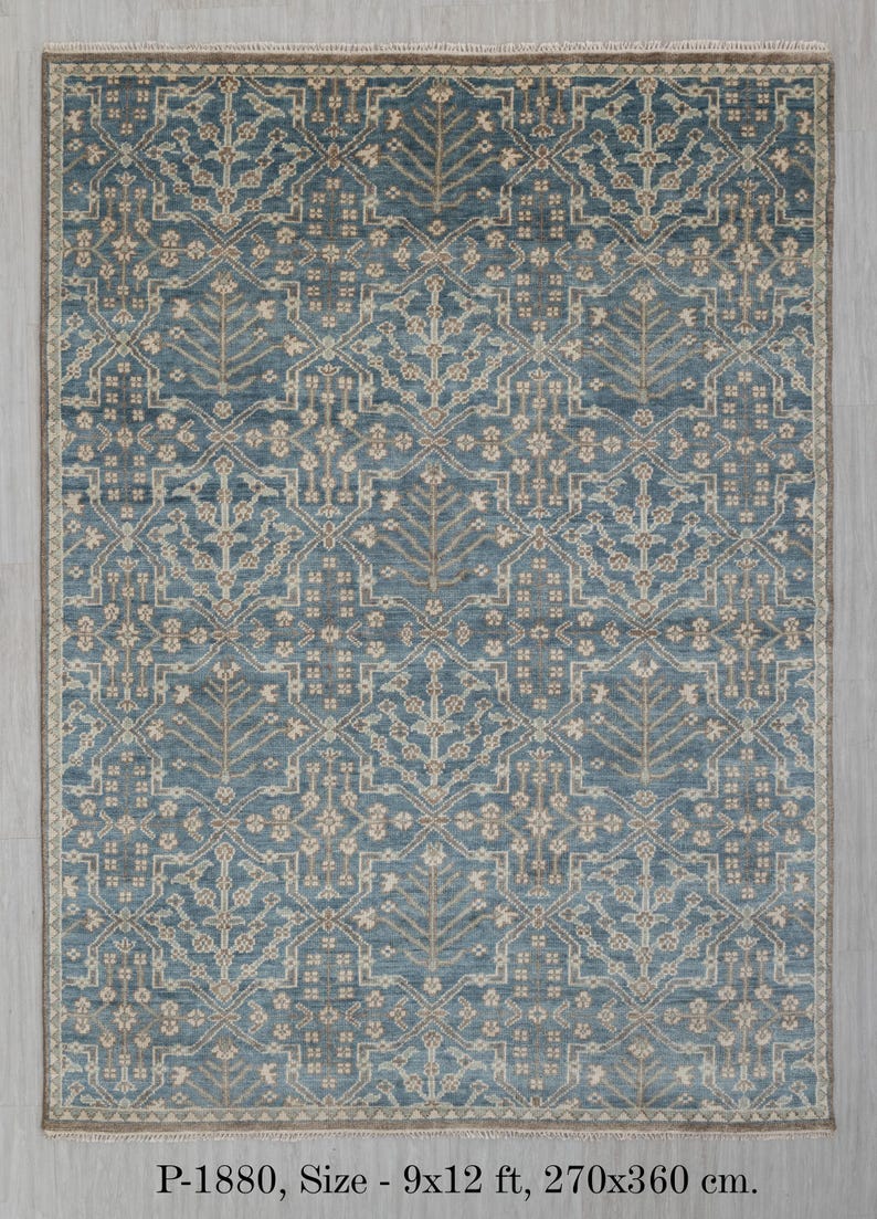 May include: A rectangular rug with a detailed, symmetrical pattern in shades of blue and beige. The rug measures 9x12 ft. The design features stylized floral and geometric elements, creating a classic and elegant look. The rug has a beige border.