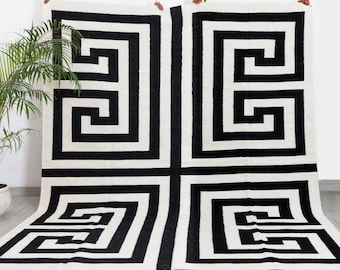 Puede incluir: Alfombra geométrica en blanco y negro con un patrón de llave griega. La alfombra está hecha de un material suave y tejido y tiene un diseño contemporáneo.