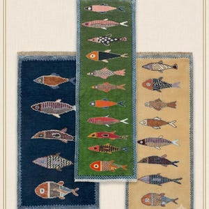 May include: Three rectangular woven rugs featuring rows of stylised fish patterns. The left rug is dark blue, the centre rug is green, and the right rug is tan. Each rug has a decorative border and fringed edges with various fish designs.