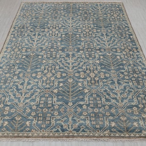 May include: A rectangular area rug with a detailed, repeating pattern in shades of blue, beige, and brown. The rug features a central design of stylized floral and geometric shapes, with a border of similar colors. The rug is suitable for living rooms and bedrooms.