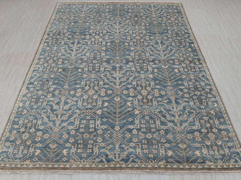 May include: A rectangular area rug with a detailed, repeating pattern in shades of blue, beige, and brown. The rug features a central design of stylized floral and geometric shapes, with a border of similar colors. The rug is suitable for living rooms and bedrooms.