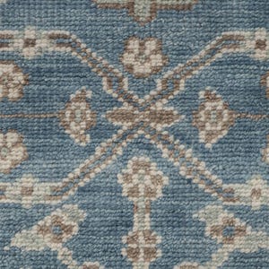 May include: Close-up of a blue rug with a detailed pattern. The design features repeating floral and geometric shapes in shades of beige and brown, creating a textured surface. The rug's color palette is a mix of blue, beige, and brown.
