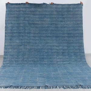 Puede incluir: Una alfombra azul y blanca a rayas con un borde de flecos. La alfombra está hecha de un material tejido y tiene un patrón sutil.