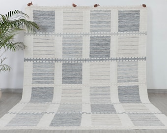 May include: A white and gray woven rug with a geometric pattern of squares. The rug has a subtle texture and a fringed edge.