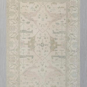 Puede incluir: Alfombra rectangular con un intrincado patrón floral y geométrico. La alfombra presenta un fondo crema con un borde y un diseño central en tonos de verde claro, rosa y beige. El diseño incluye motivos florales estilizados y formas geométricas.