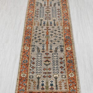 May include: A rectangular, beige runner rug with an intricate pattern. The design features repeating floral and geometric motifs in shades of orange, blue, and white. The rug has a border with a similar color palette.