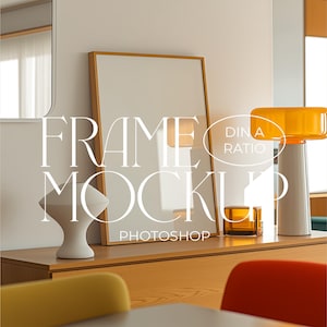 Puede incluir: Maqueta de marco vertical con marco de madera, apoyada contra una pared. La imagen incluye un jarrón blanco, un pequeño cubo de vidrio ámbar y una lámpara moderna con pantalla naranja. El texto "FRAME MOCKUP PHOTOSHOP" es visible.