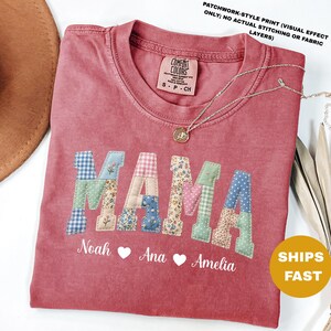 以下が含まれることがあります： パッチワーク風の文字で「MAMA」と書かれた赤いComfort ColorsのTシャツ。名前のNoah、Ana、Ameliaが下に書かれています。金のネックレスがTシャツの上にあります。Tシャツには「SHIPS FAST」の文字があります。