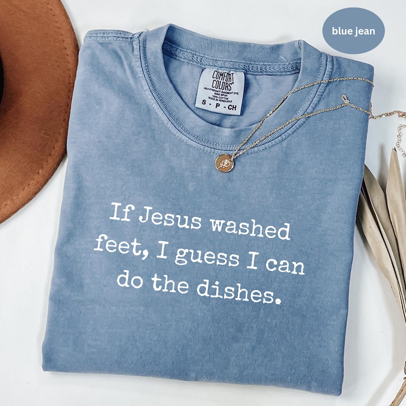 May include: A blue jean Comfort Colors t-shirt with the text "If Jesus washed feet, I guess I can do the dishes." A gold necklace with a pendant is on the shirt.
