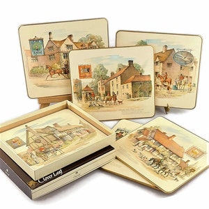 May include: Set of vintage Clover Leaf placemats featuring detailed illustrations of English pubs and inns. The placemats have a rectangular shape with a gold trim. The set includes a box with the Clover Leaf logo.