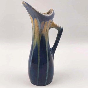 Peut inclure: Un petit pichet en céramique bleu et or avec un bec évasé et une anse. Le pichet a une finition émaillée avec un motif strié.